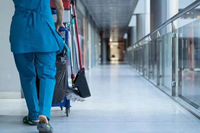 Eine Reinigungskraft schiebt ihren Wagen in einem Flur bei der Arbeit in einem Gewerbegebäude