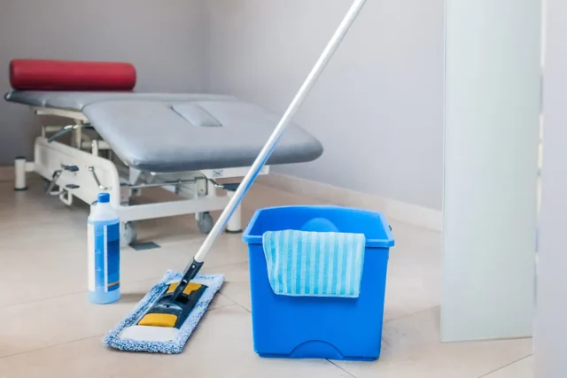 Schrubber, Putzmittel und Putzeimer stehen bereit in einem Behandlungsraum für die Praxisreinigung